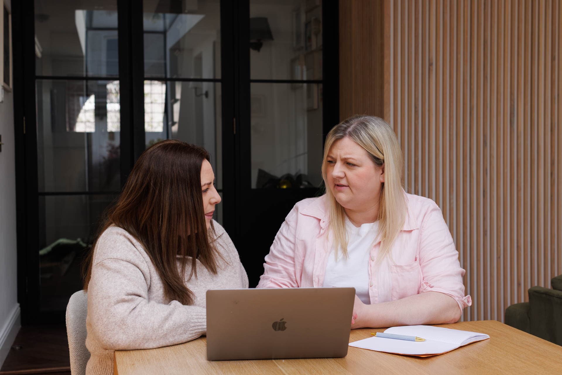 Two women engaged in conversation in a well-lit room discuss a reciprocal IVF treatment